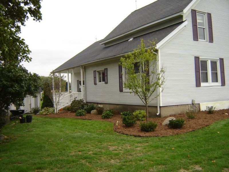 Two-story house with gray siding, purple shutters, and landscaped yard with mulch and shrubs.