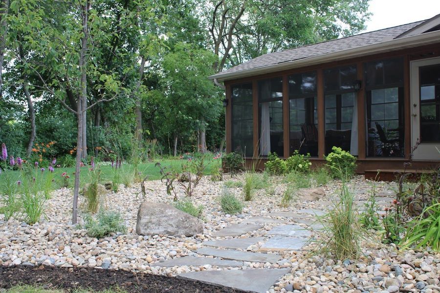 Stone path through a landscaped yard with a house and screened porch in the background.