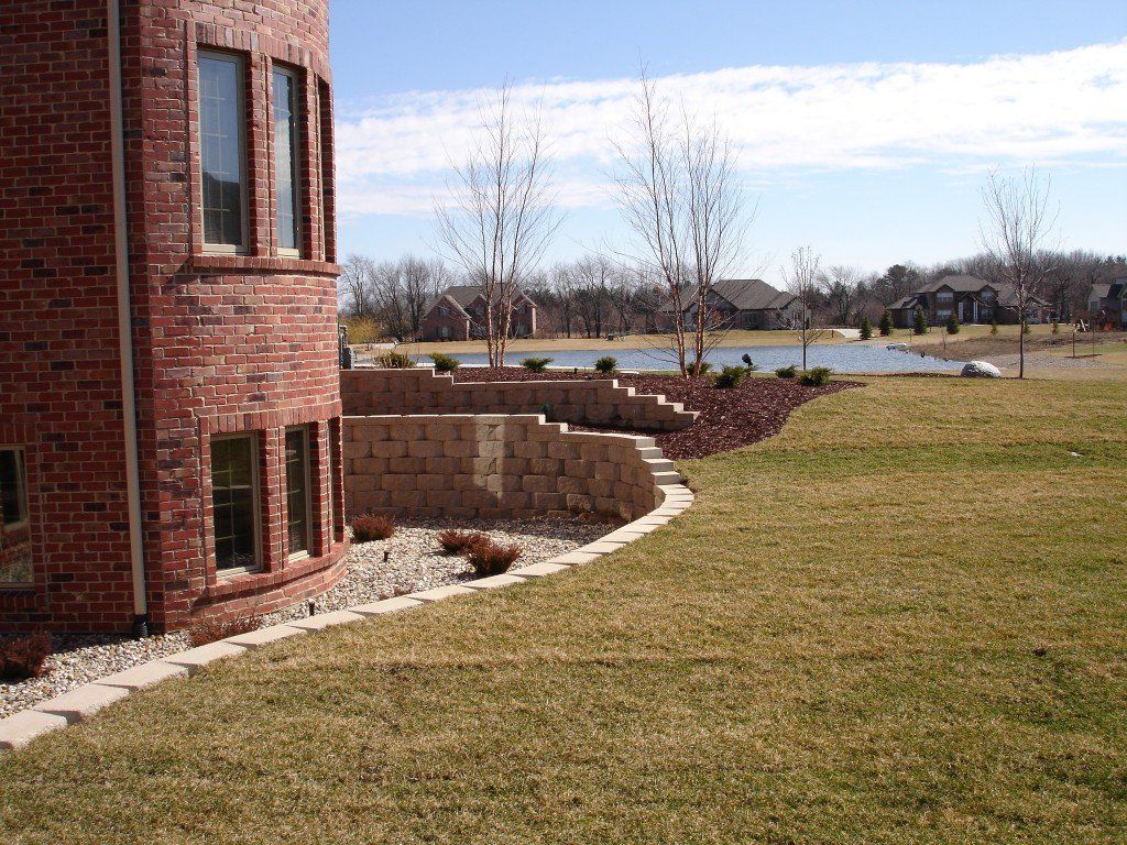 Brick house exterior with tiered retaining wall and lake in the background.
