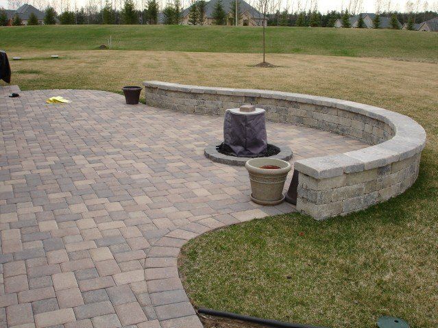 Brick patio with curved stone wall and fountain, set in a grassy yard.