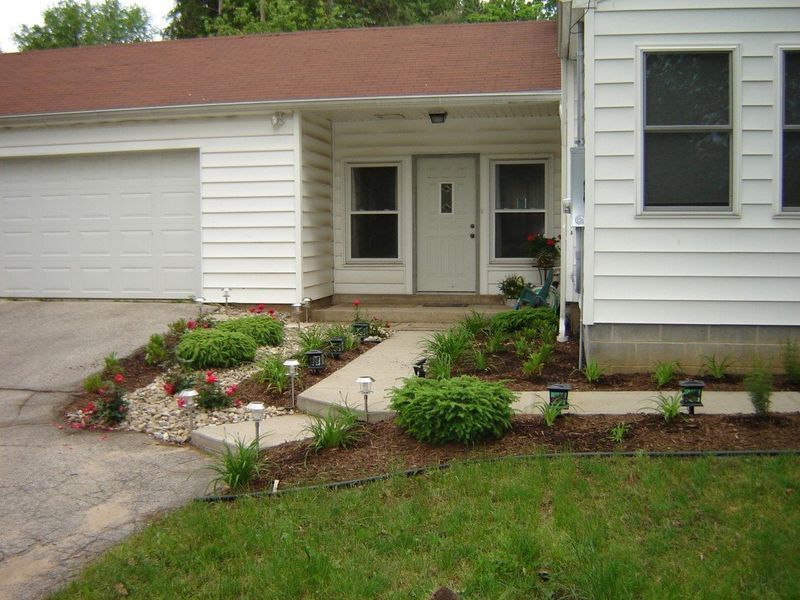 White house with a concrete walkway and landscaped front yard with flowers and solar lights.