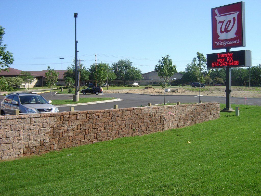 Walgreens store exterior with sign and brick wall in front of a parking lot and grass.