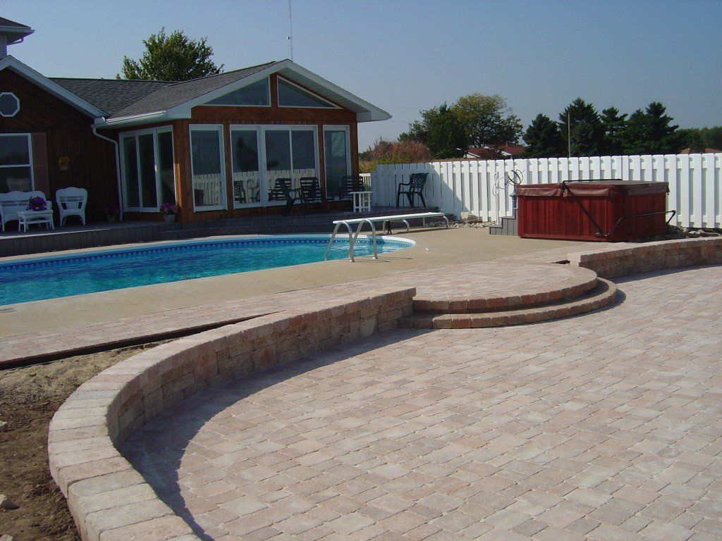 Brick patio with pool, hot tub, and house in background.