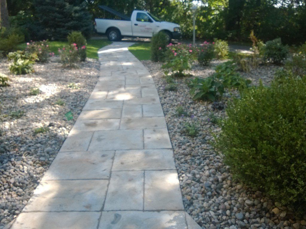 Stone pathway through a garden with a truck in the background. Gravel and plants flank the path.