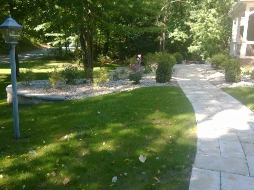 Stone pathway winds through a grassy yard with landscaping and trees.