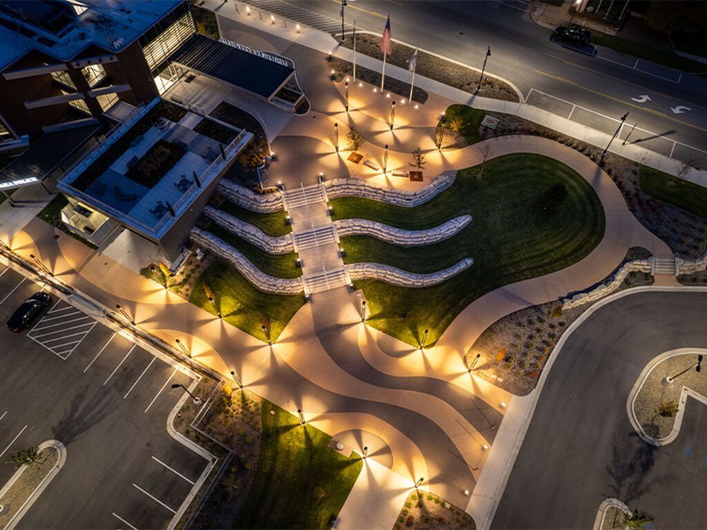 An aerial night view of a landscaped courtyard with illuminated walkways and stone-accented green spaces near a building.