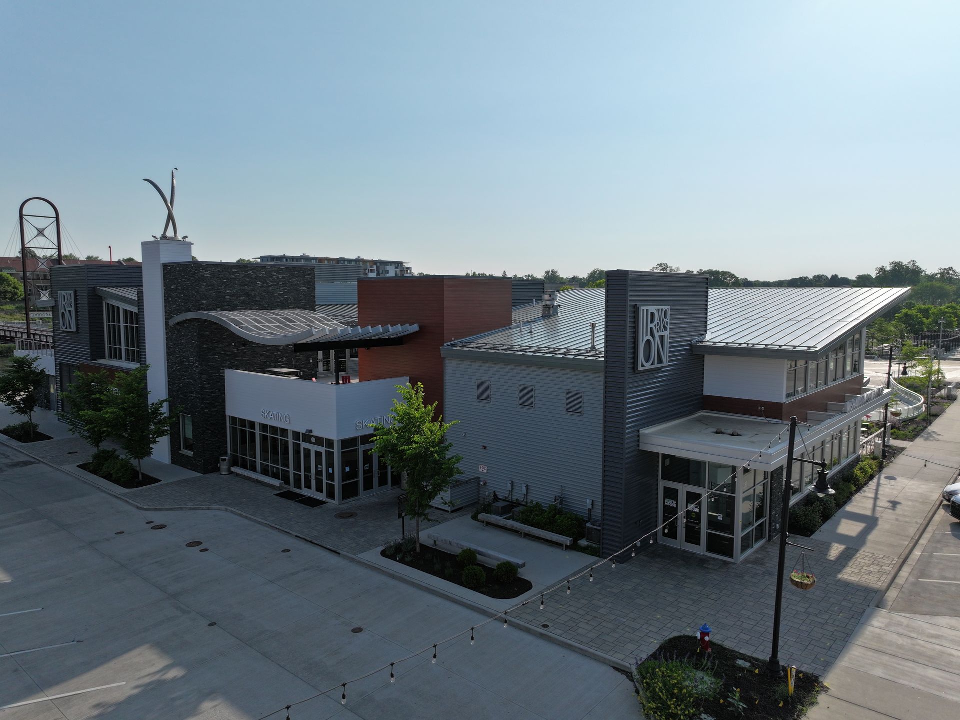 Modern, multi-section commercial building with dark, light gray, and brick exteriors under a clear blue sky.