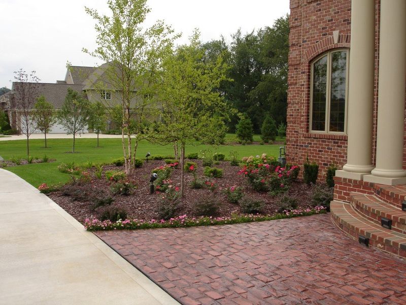 Landscaped front yard with brick walkway, red brick house, and trees.