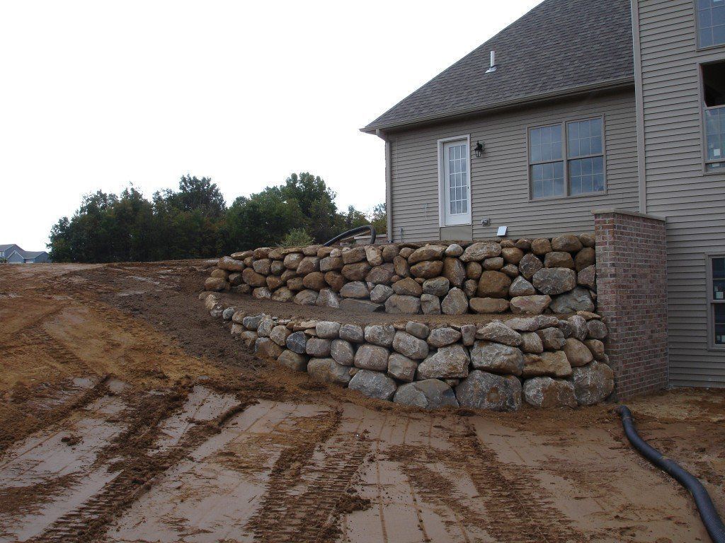 Stone retaining walls built along a house with dirt and mud in the foreground.