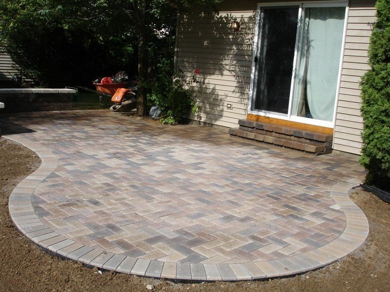 Brick patio with curved edges next to a house with a sliding glass door.