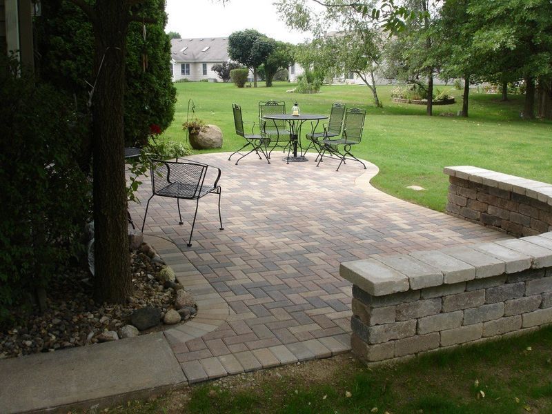 Brick patio with outdoor table and chairs, bordered by a low wall and lawn.