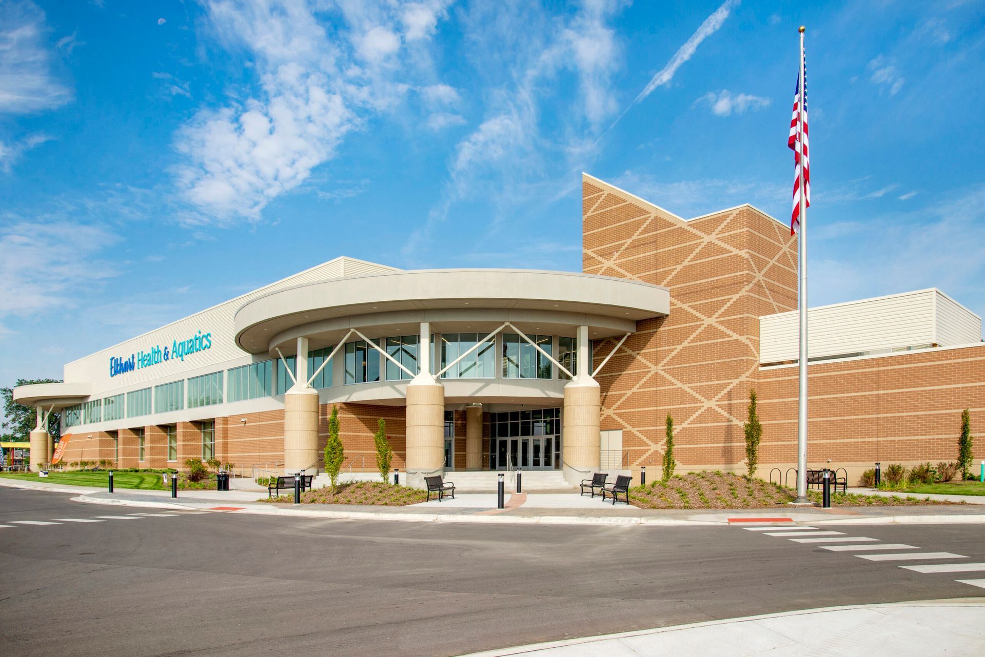 Modern brick building with a circular glass entrance and a tall American flag on a sunny day.