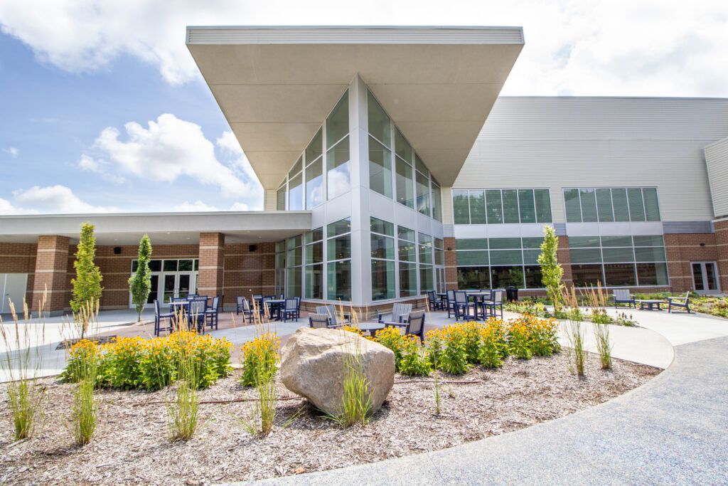 A modern building with a tall glass atrium and wide, overhanging roof, surrounded by landscaping and a stone patio.
