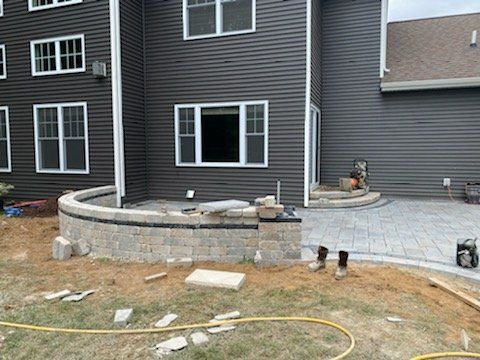 Backyard patio construction with retaining wall and gray siding.