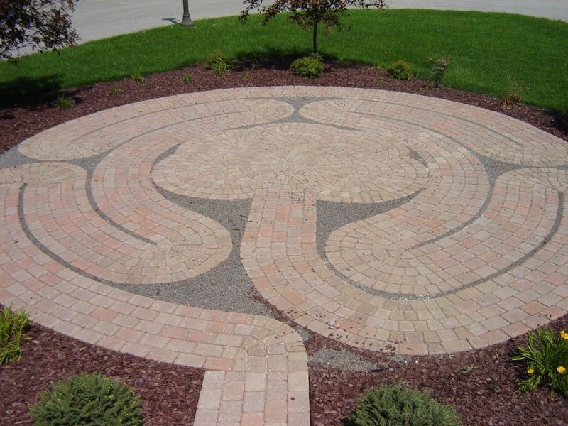 Circular brick labyrinth in a garden setting, with red brick path and dark mulch.