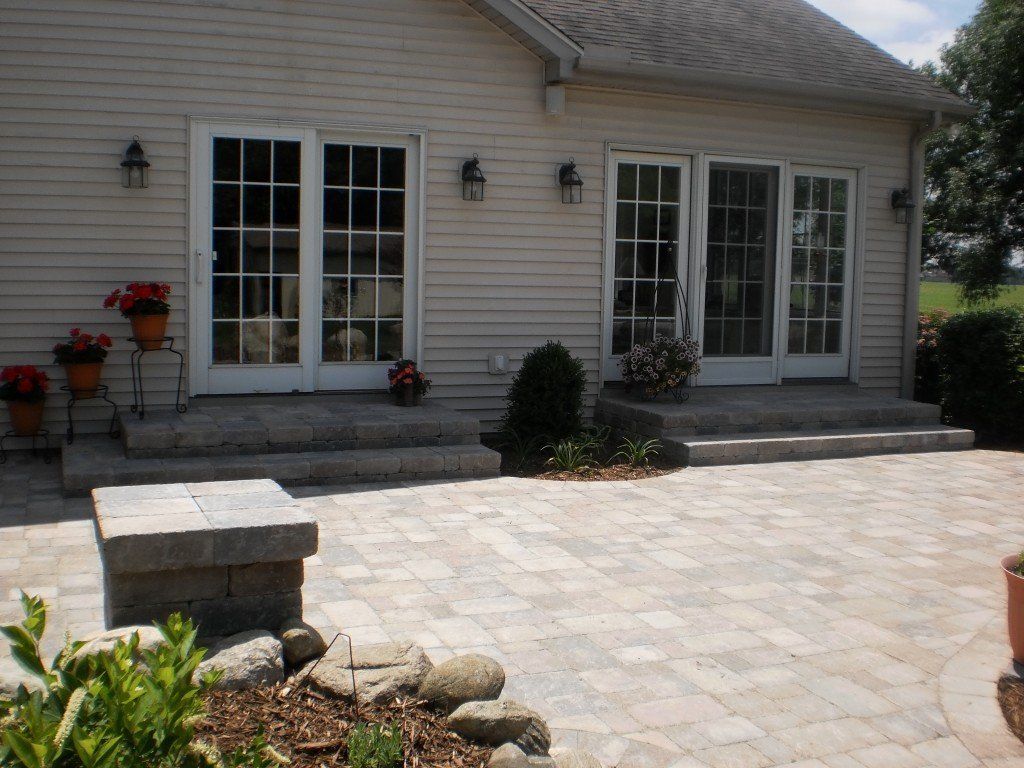 A light-colored house with French doors opens onto a paved patio with stone steps and flowerpots.