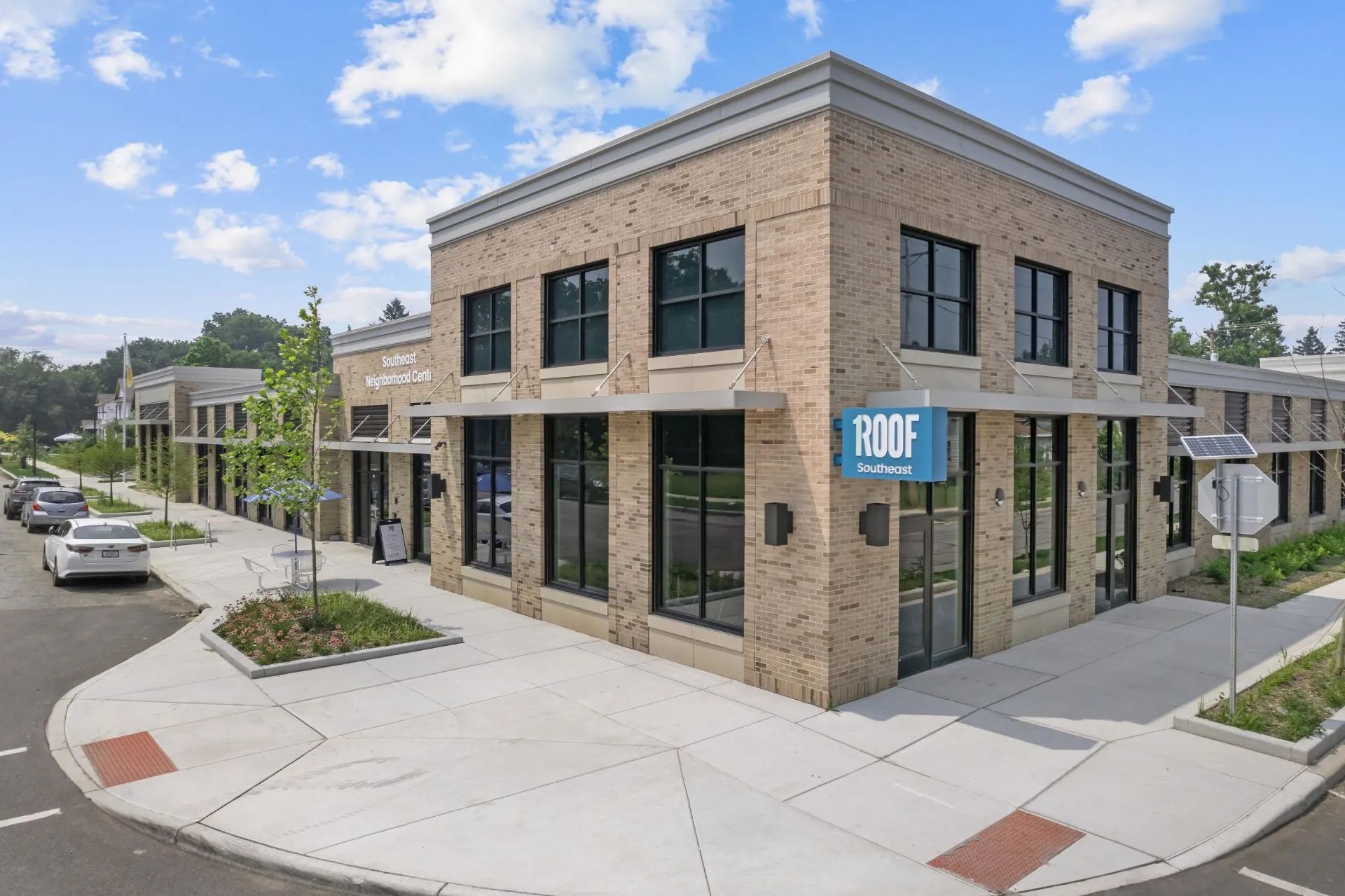 A modern, single-story tan brick retail building with large dark-framed windows and a blue 