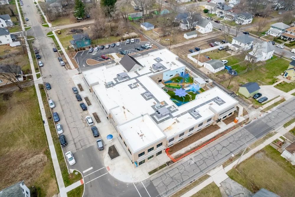 Aerial view of a U-shaped building with a central courtyard and playground, surrounded by city streets and houses.