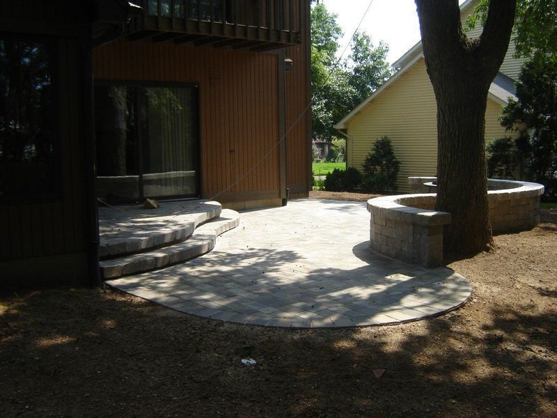 Patio with stone pavers, steps, and a circular wall around a tree; next to a house.