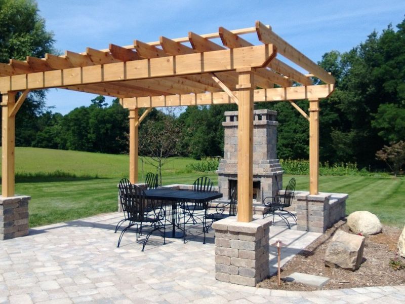 Pergola with seating area, fireplace, and stone patio in a grassy outdoor setting.
