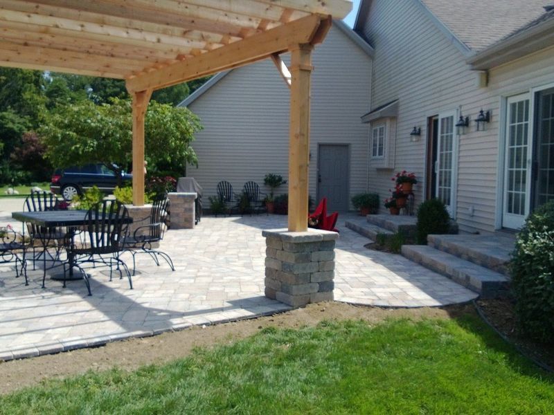 Patio with pergola, stone pavers, outdoor dining set, and house with steps.