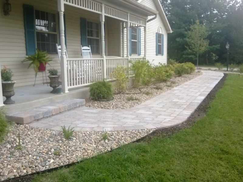 A paved walkway leads from a porch to the lawn. Gravel and landscaping border the path.