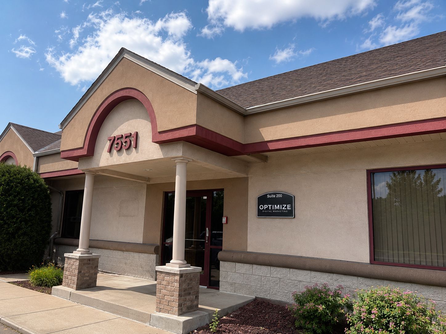 Single-story beige storefront with red trim, columns, and a sign near the entrance under a blue sky.