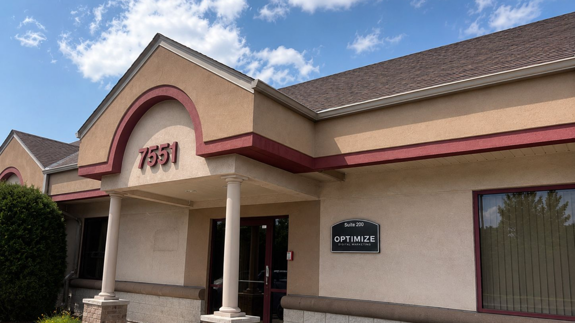Tan stucco office building with arched entrance and maroon trim under a blue sky