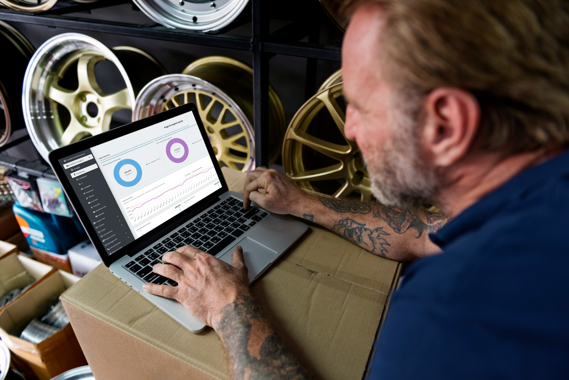 Man using a laptop beside stacked car wheels in a workshop, viewing charts on the screen