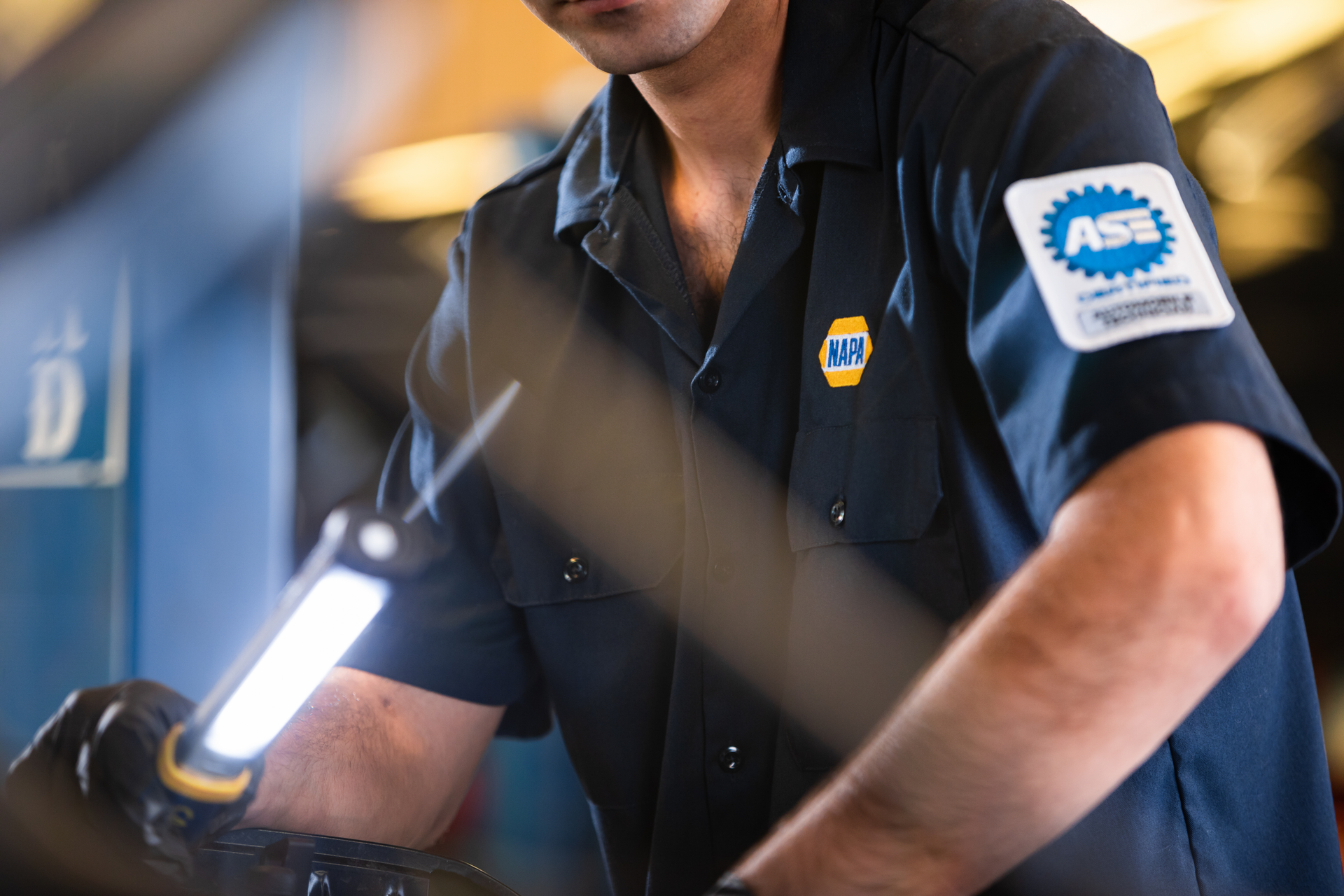 Mechanic in dark uniform working on a vehicle with a tool in a garage