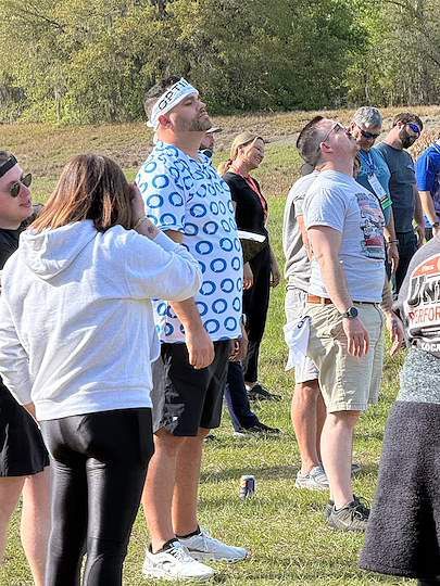 People standing outdoors on grass, gathered in a sunny park during an event
