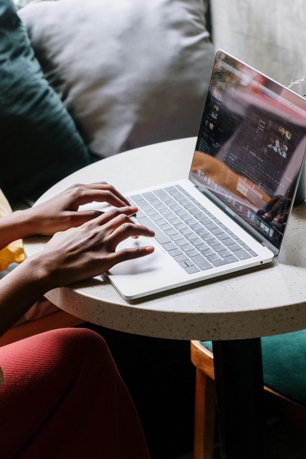 Hands typing on a laptop at a small round table beside a couch.