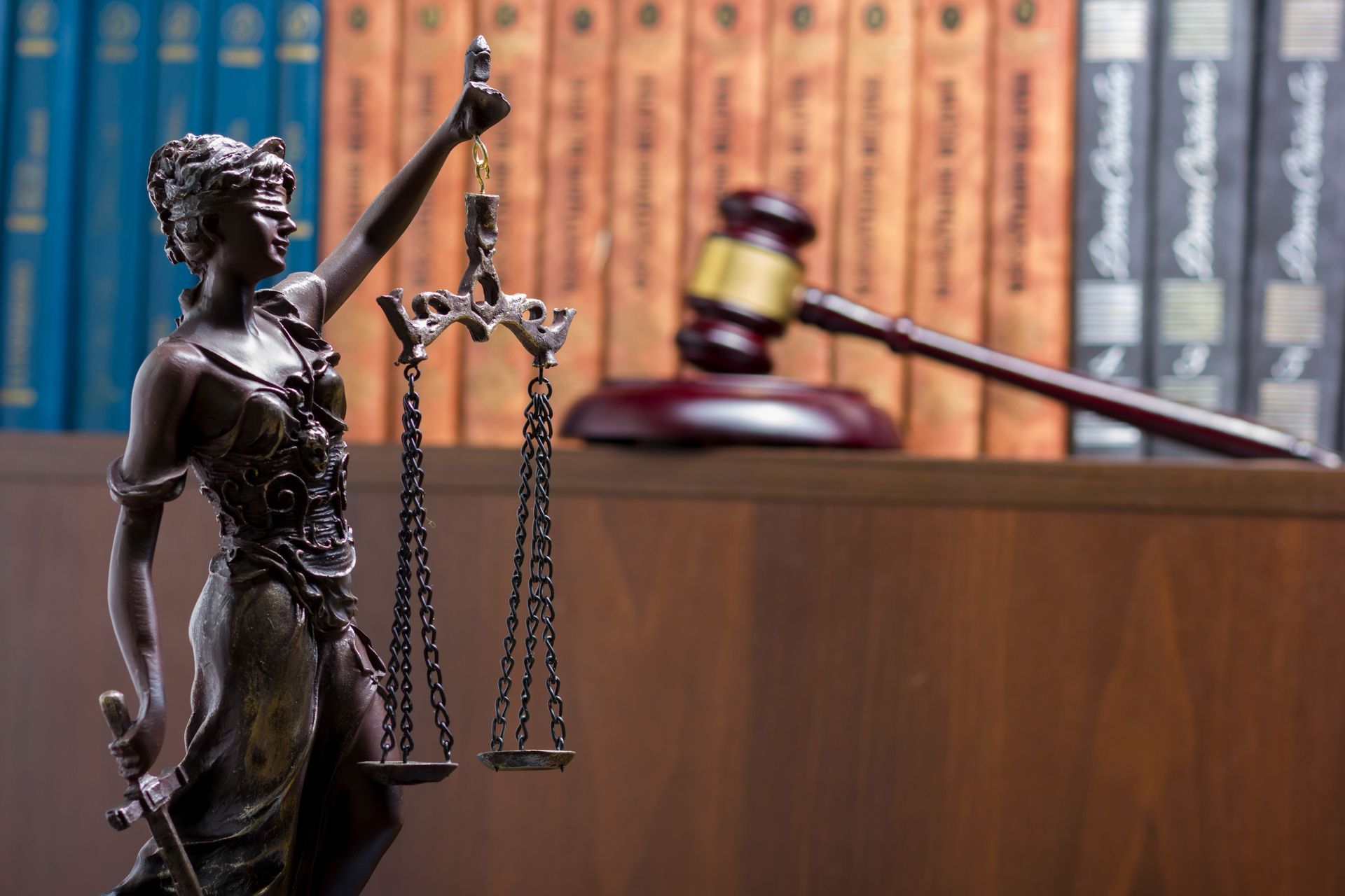 Bronze Lady Justice statue in front of law books and a judge’s gavel on a desk