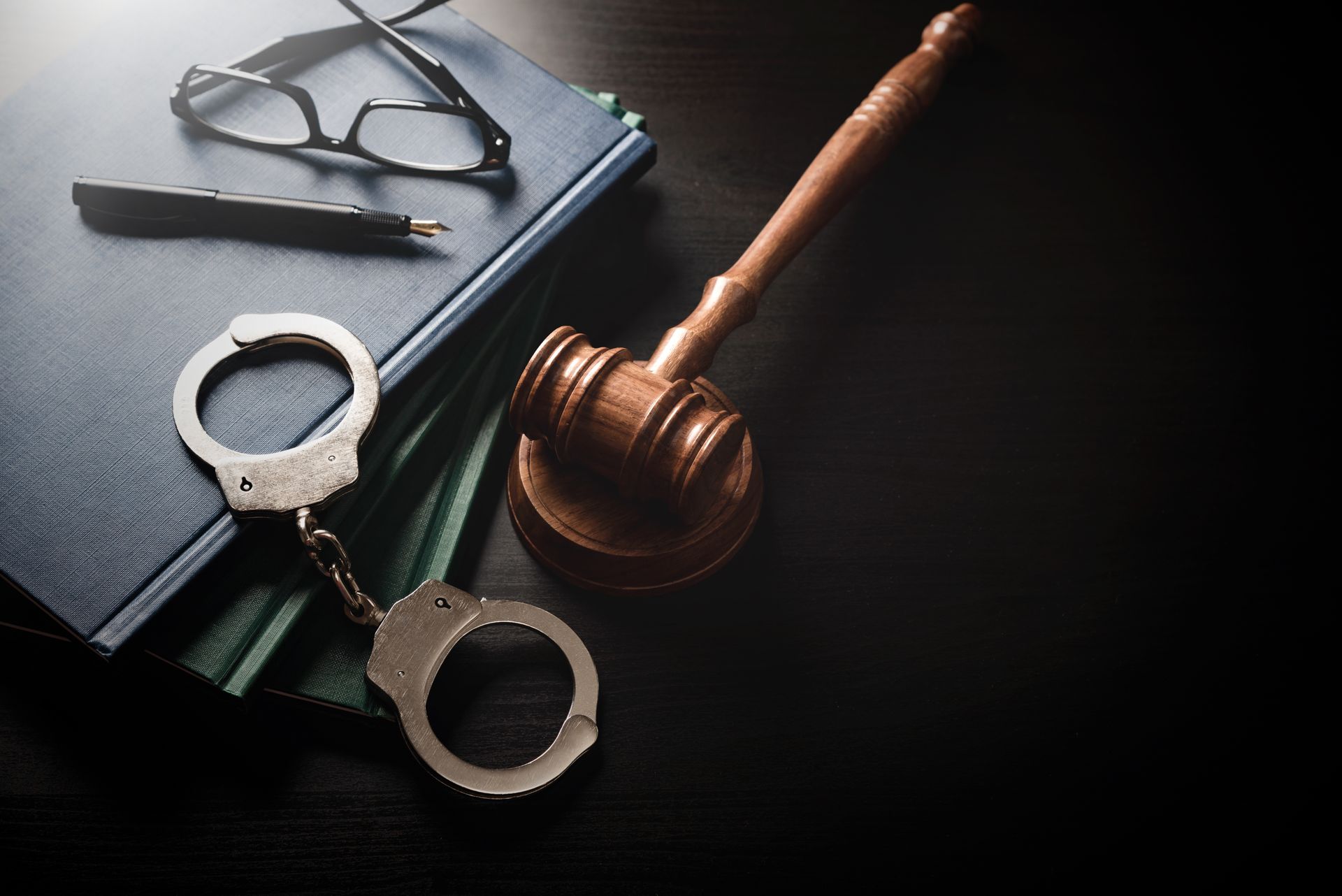 Gavel, handcuffs, and eyeglasses on a dark desk, suggesting law and justice