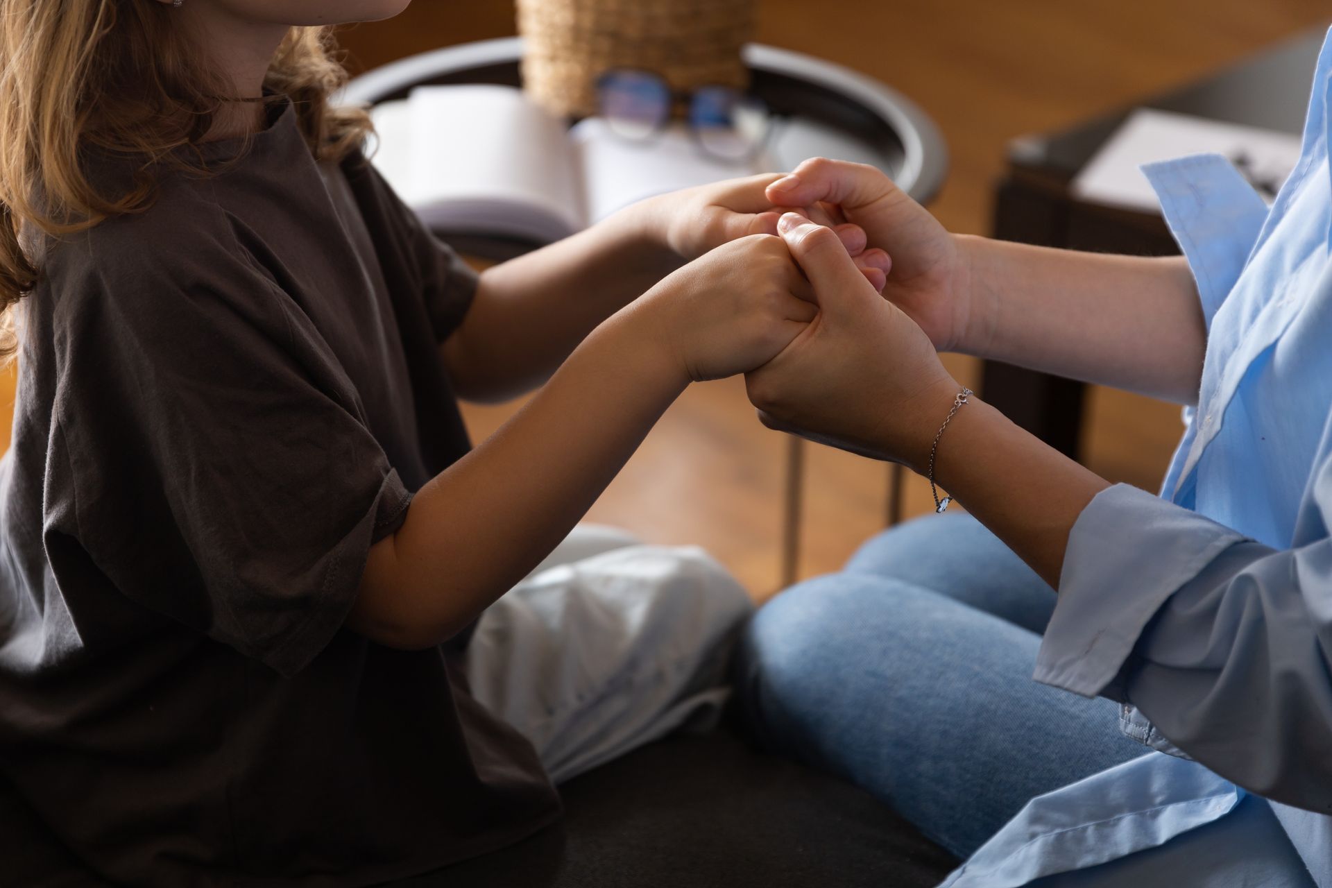 Two people seated closely, holding hands in a supportive gesture indoors