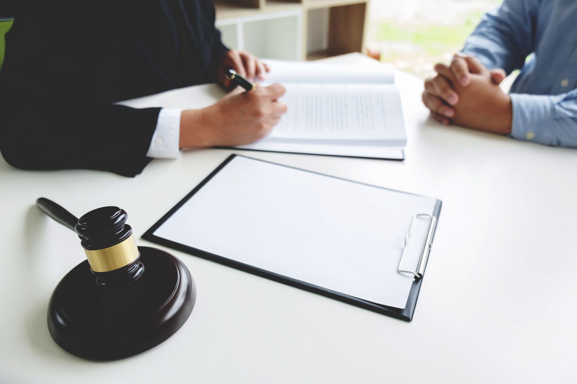Two people in a business meeting signing documents at a white table with a clipboard and stamp