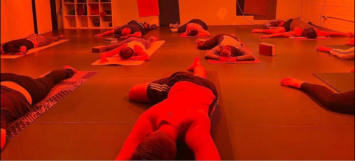 People lying on mats in a red-lit exercise or relaxation room