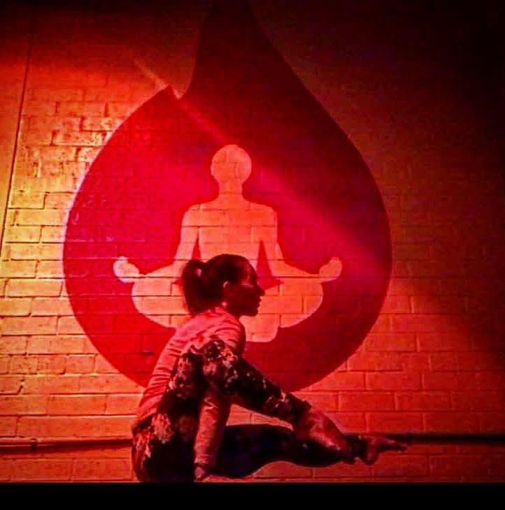 Person sitting in meditation pose before a red flame-like mural on a brick wall