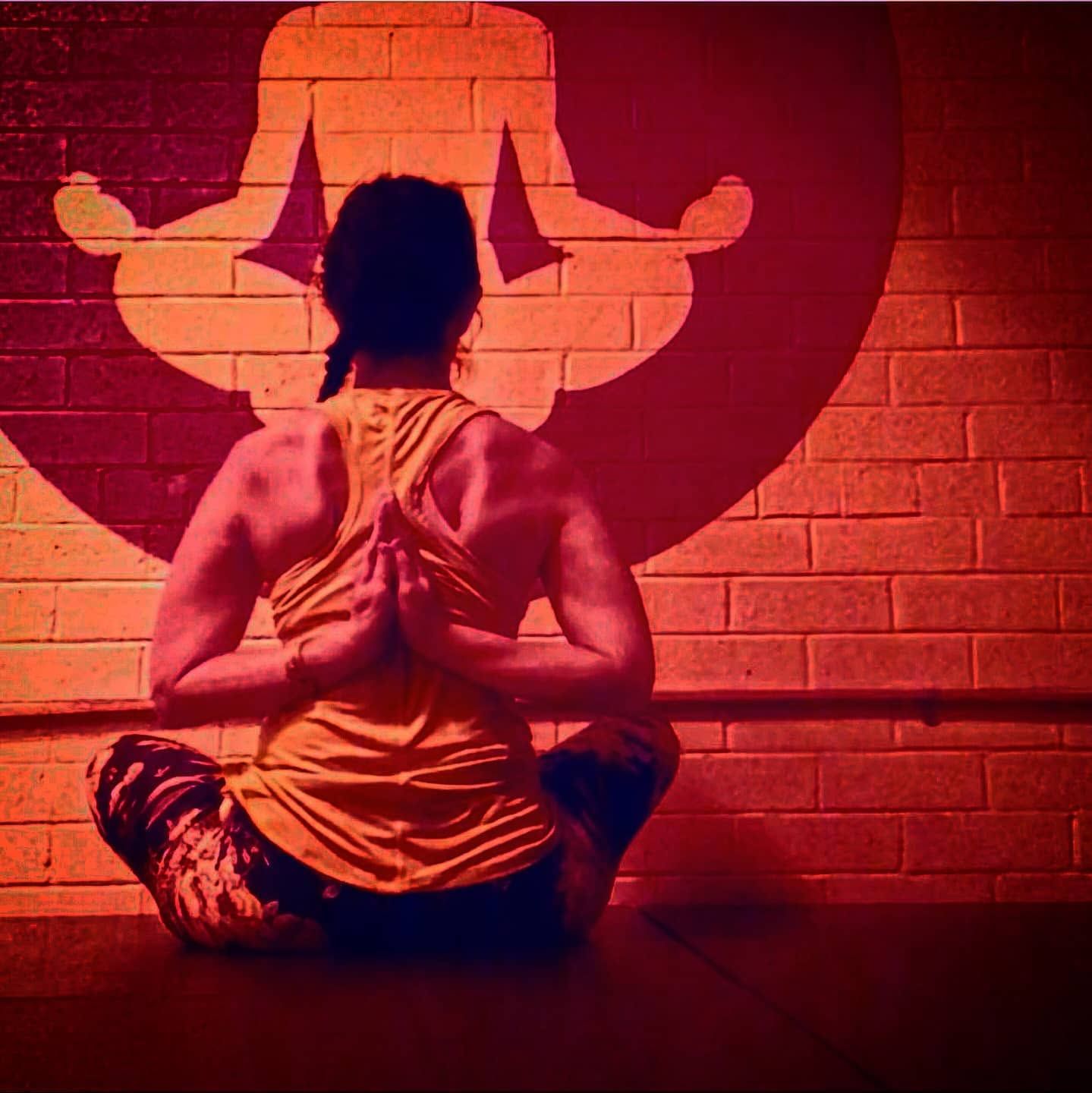 Person meditating cross-legged on a mat before a red brick wall with a yoga symbol.