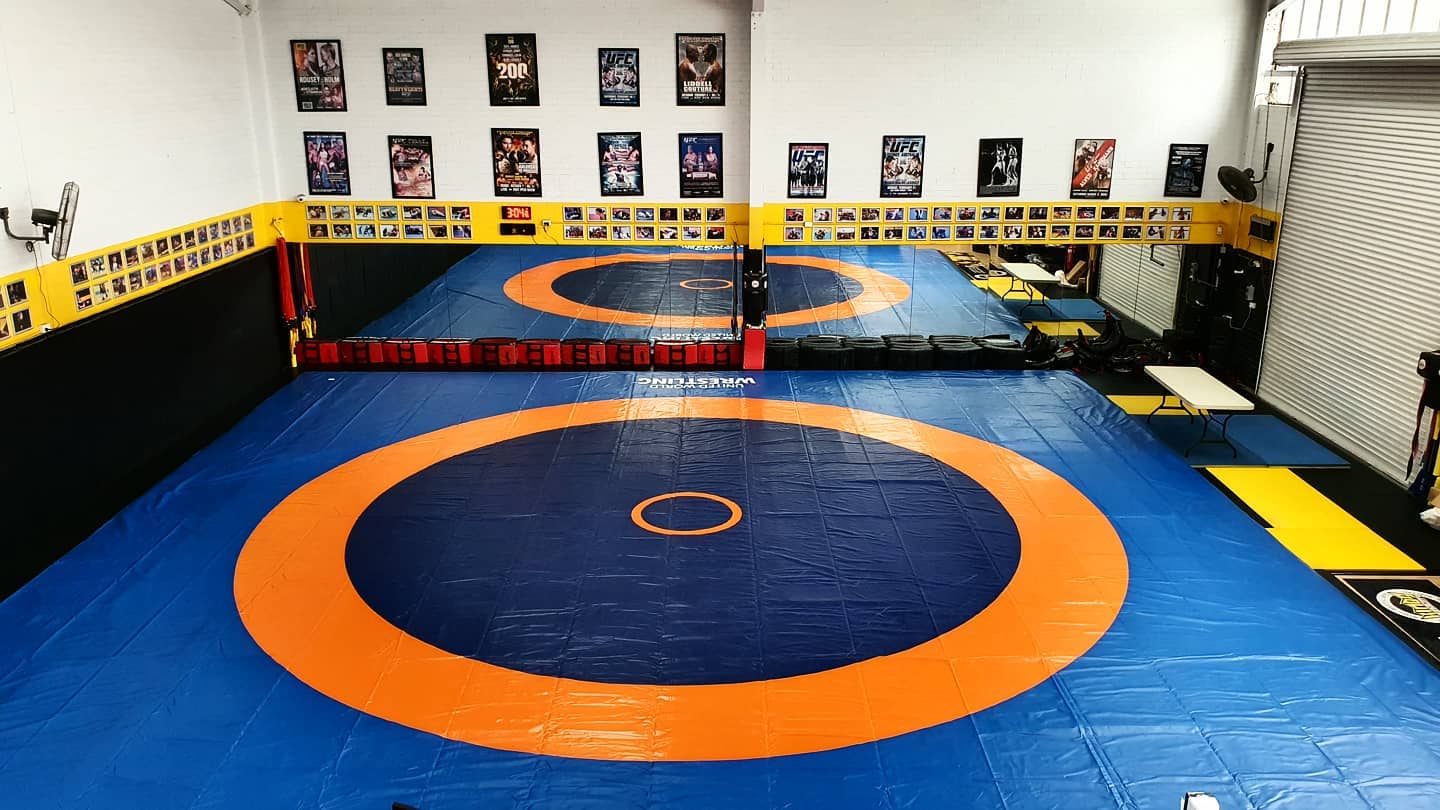 Blue and orange wrestling mat in a training room with wall posters and caution tape borders