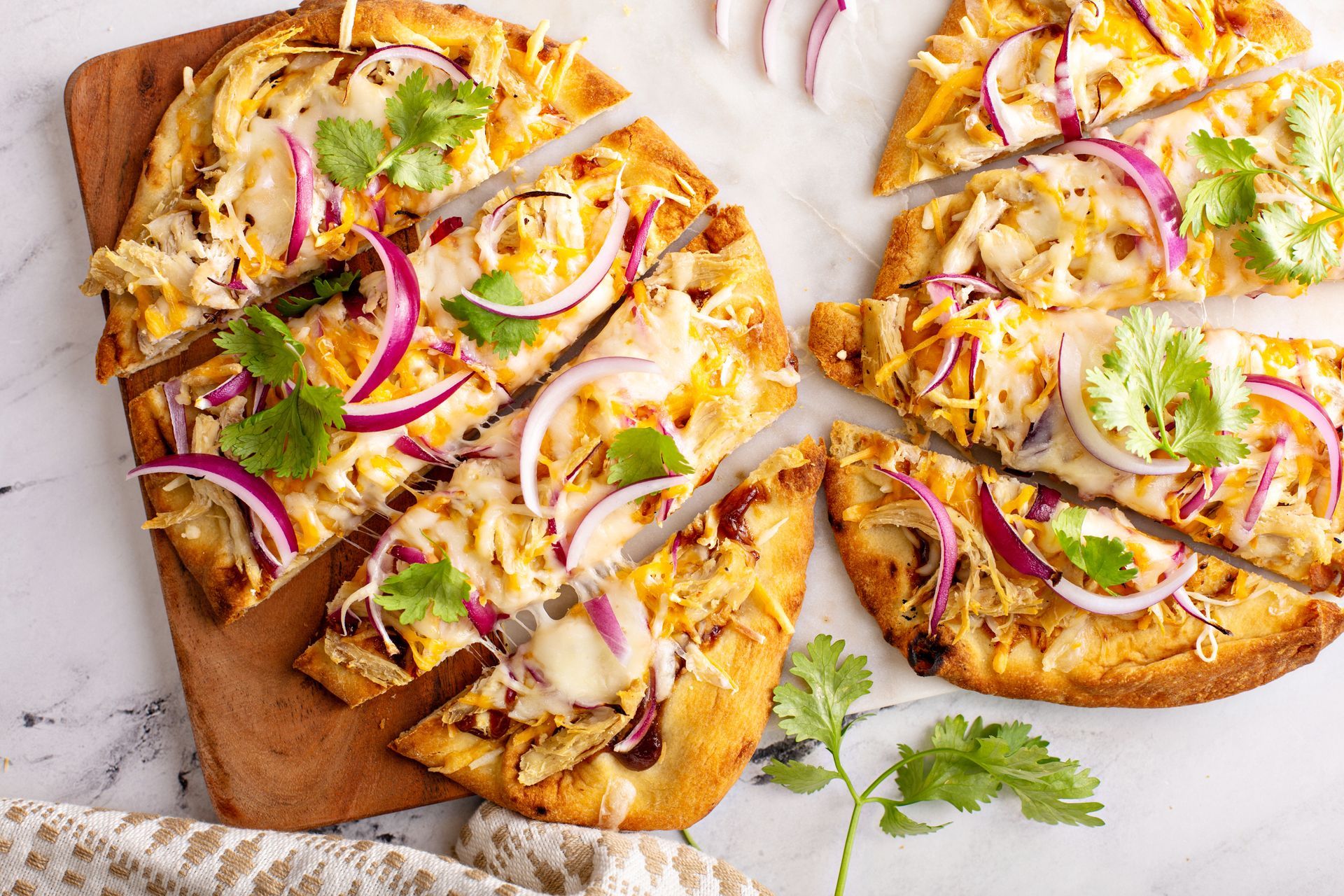 A pizza with onions and cilantro is sitting on a wooden cutting board.
