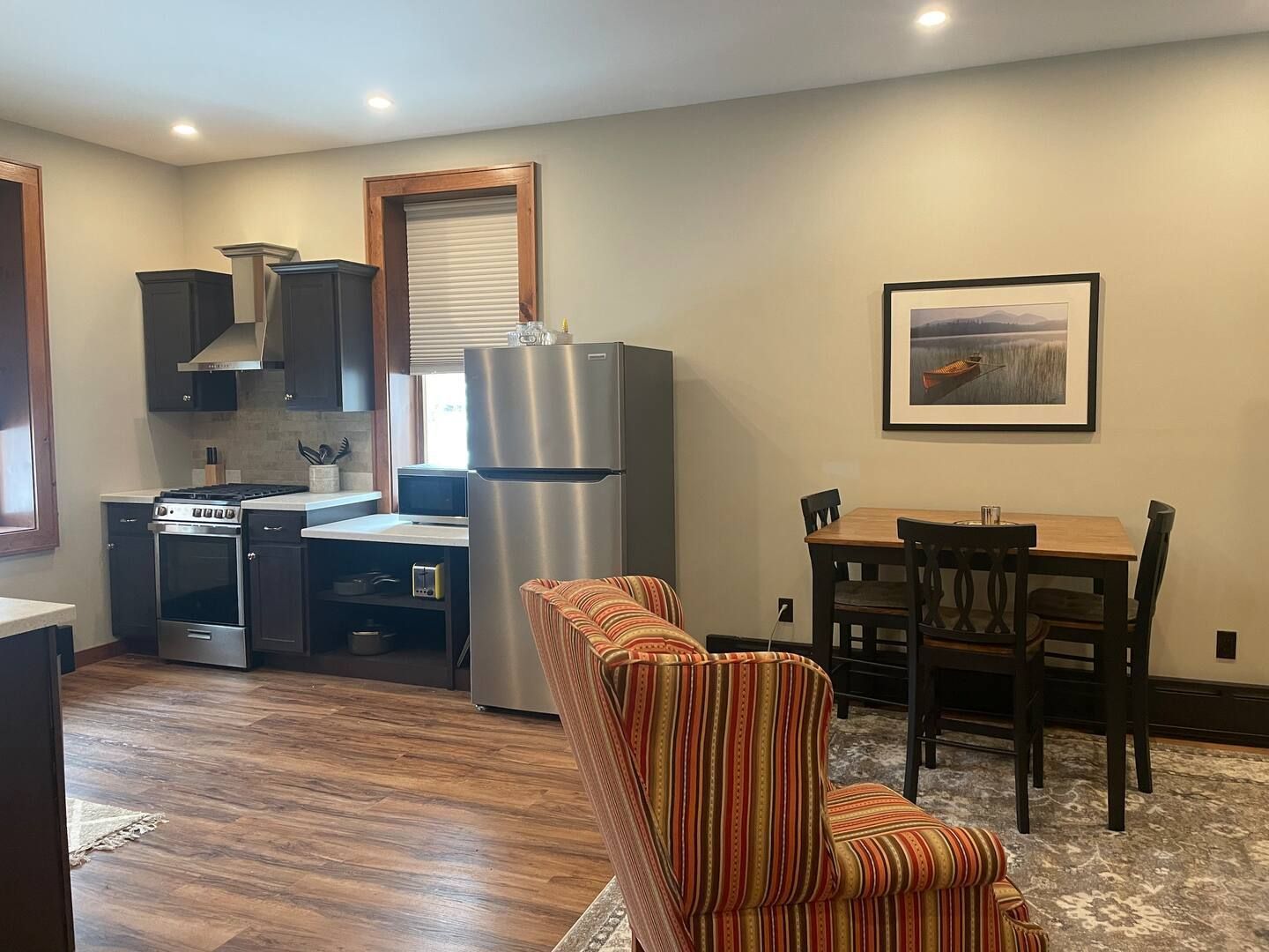 A living room with a stainless steel refrigerator , table and chairs.