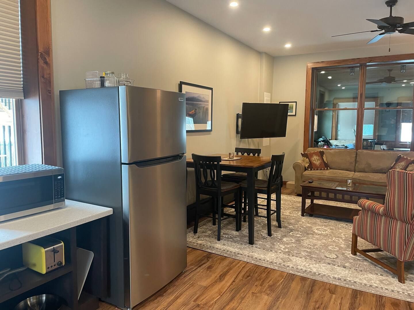 A living room with a stainless steel refrigerator , dining table , chairs and a couch.