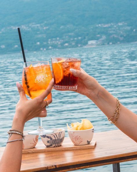 Donna che si rilassa su una sedia a sdraio con un drink e una borsa rossa, con vista sull'acqua.