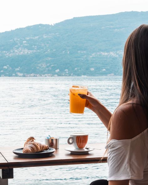 Tavolo per la colazione con croissant, pasticcini, caffè e succo d'arancia, con vista sul lago.