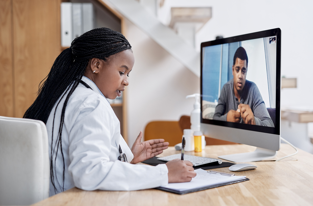 A doctor is sitting at a desk talking to a patient on a video call.
