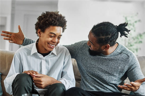 Two men are sitting on a couch talking to each other.