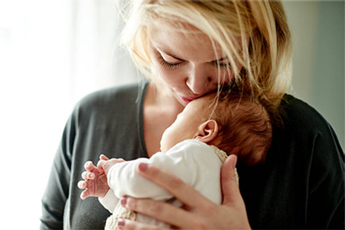 A woman is holding a baby in her arms and kissing it on the cheek.