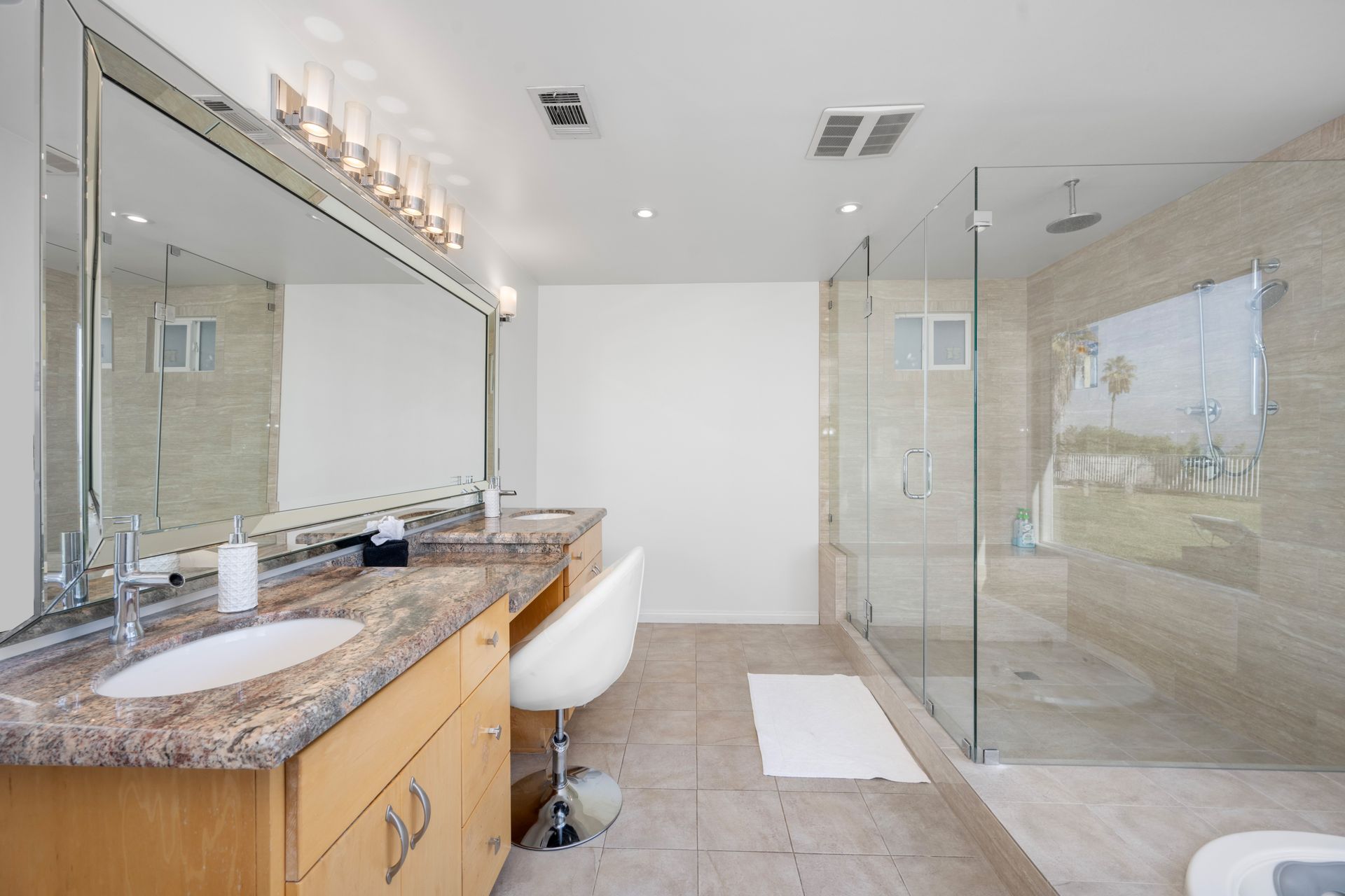 Modern bathroom with double vanity, large mirror, glass shower, and marble countertops.