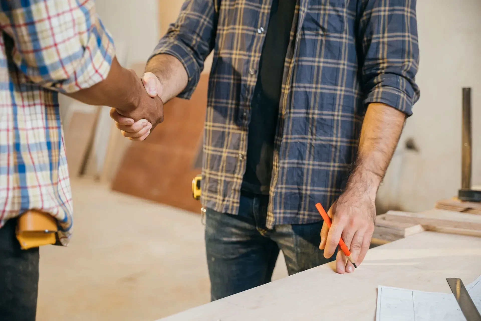 Two people shaking hands in a workshop, one holding orange-handled pliers beside a workbench.